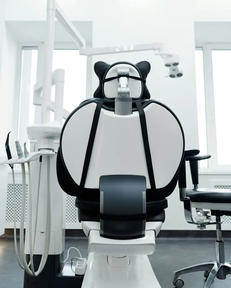 A bright treatment room with a white and black dental chair between two windows.