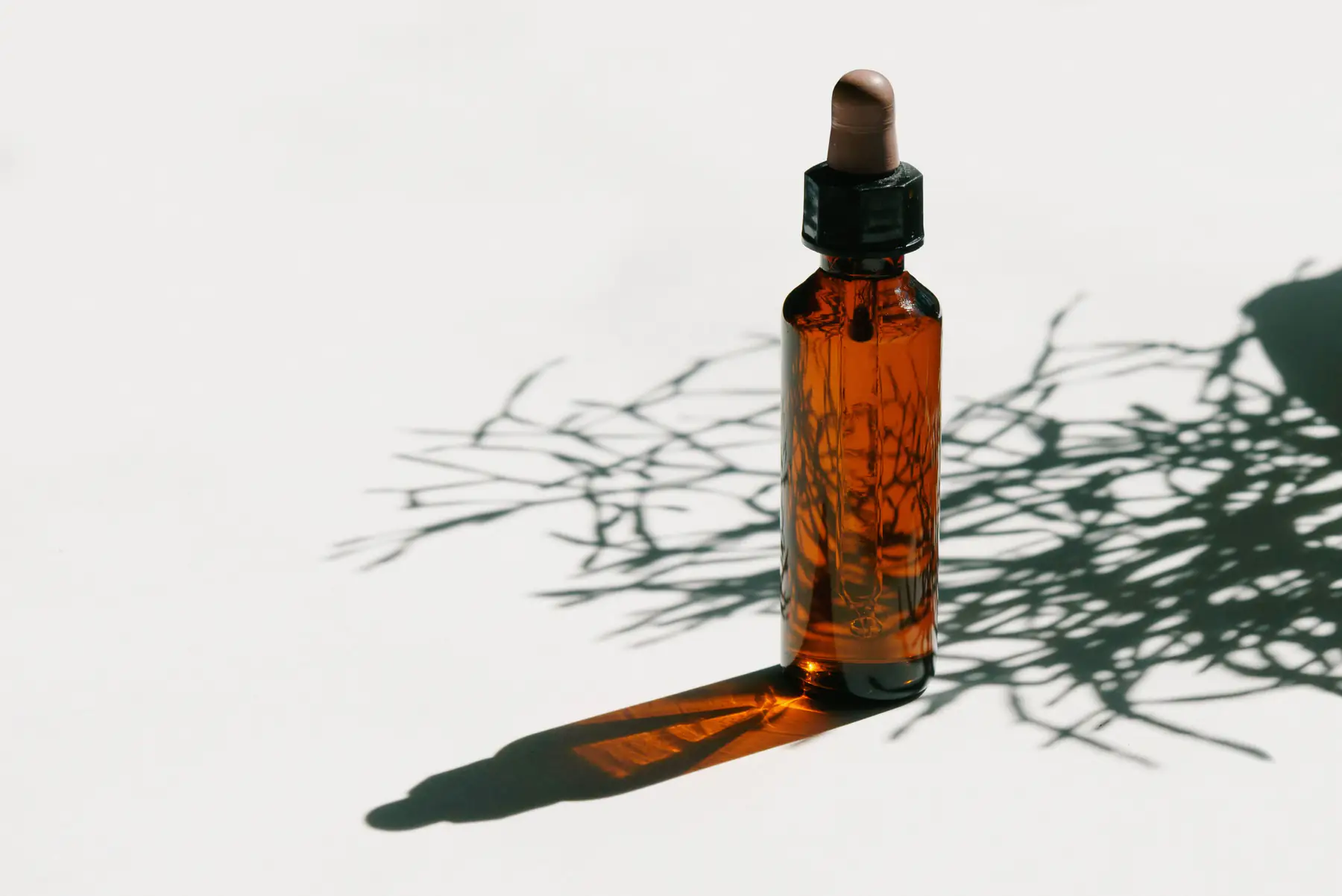Rain Serum standing on a white table, with the shadows of leaves around it